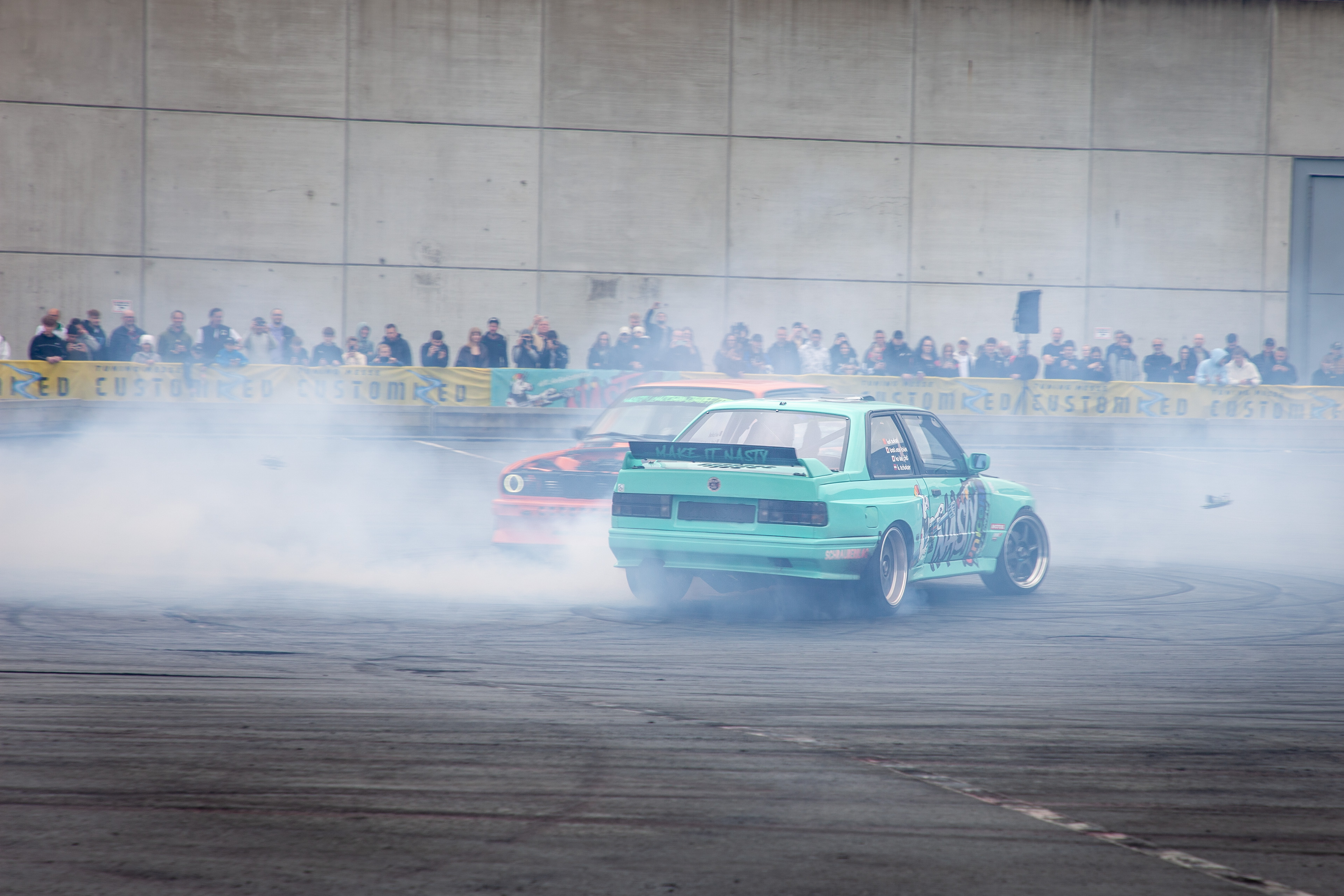 Zwei BMW E30 Driftautos im Doppel-Drift vor Publikum