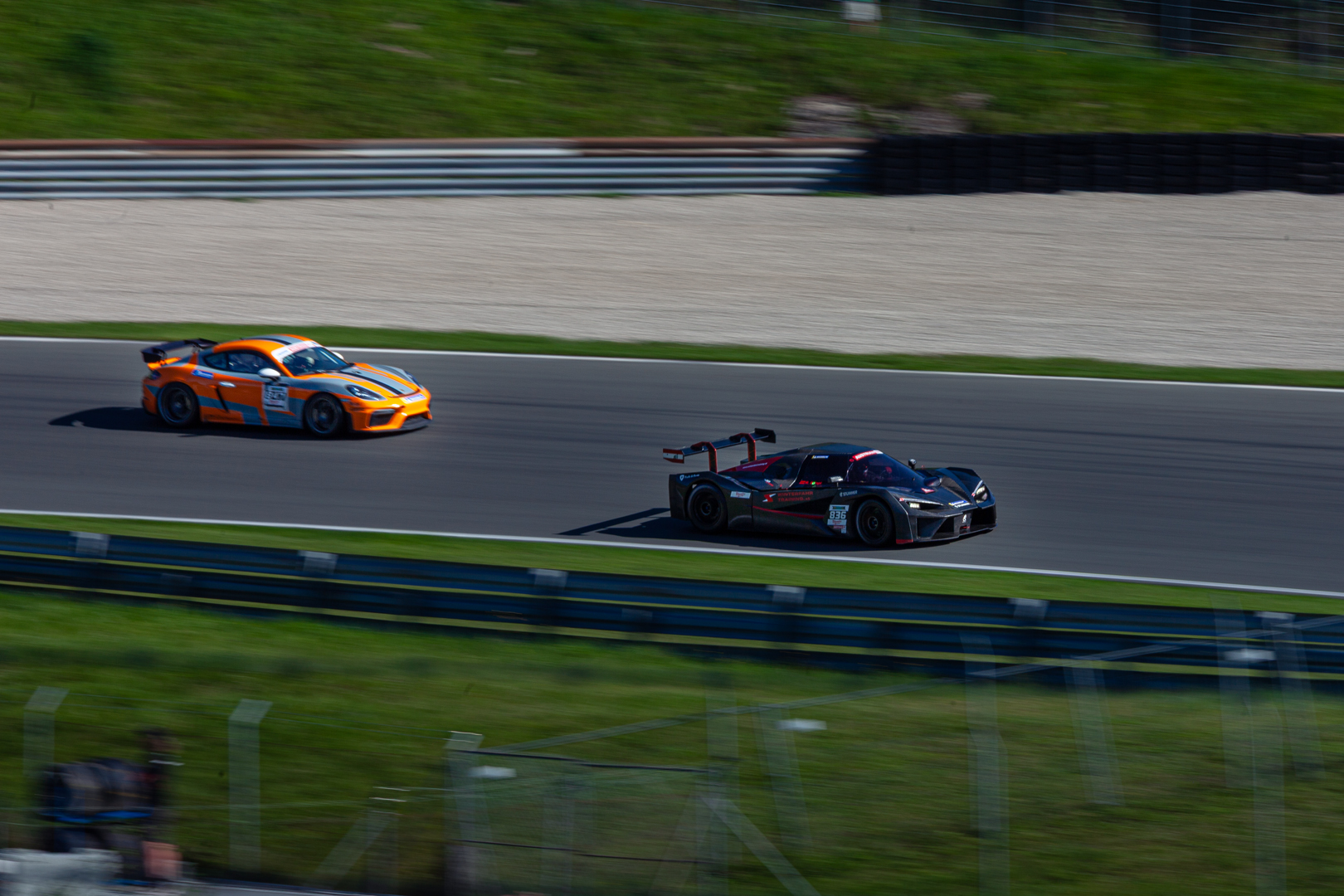 Orangefarbener Porsche Cayman GT4 und schwarzer Prototyp auf der Rennstrecke