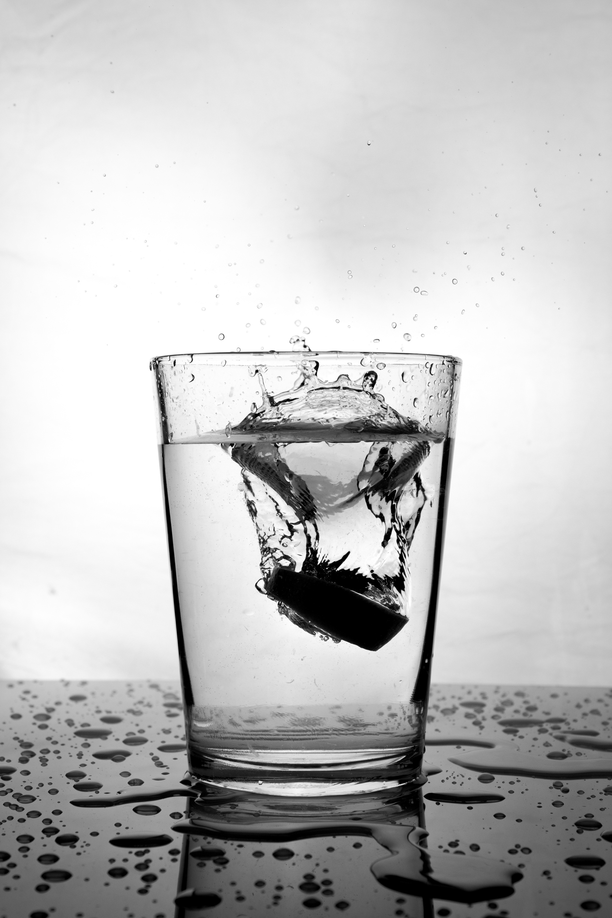 Schwarzes Objekt spritzt in ein Wasserglas, Schwarz-Weiß
